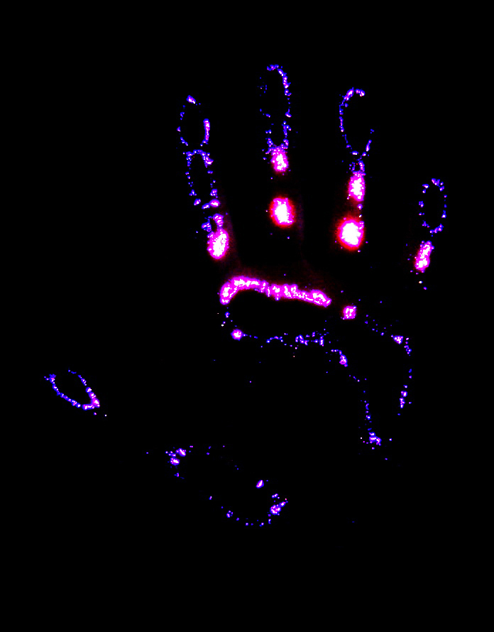 Photographie Kirlian d'une main entière : couronnes violettes et magenta autour des doigts et de la paume, sur fond noir.